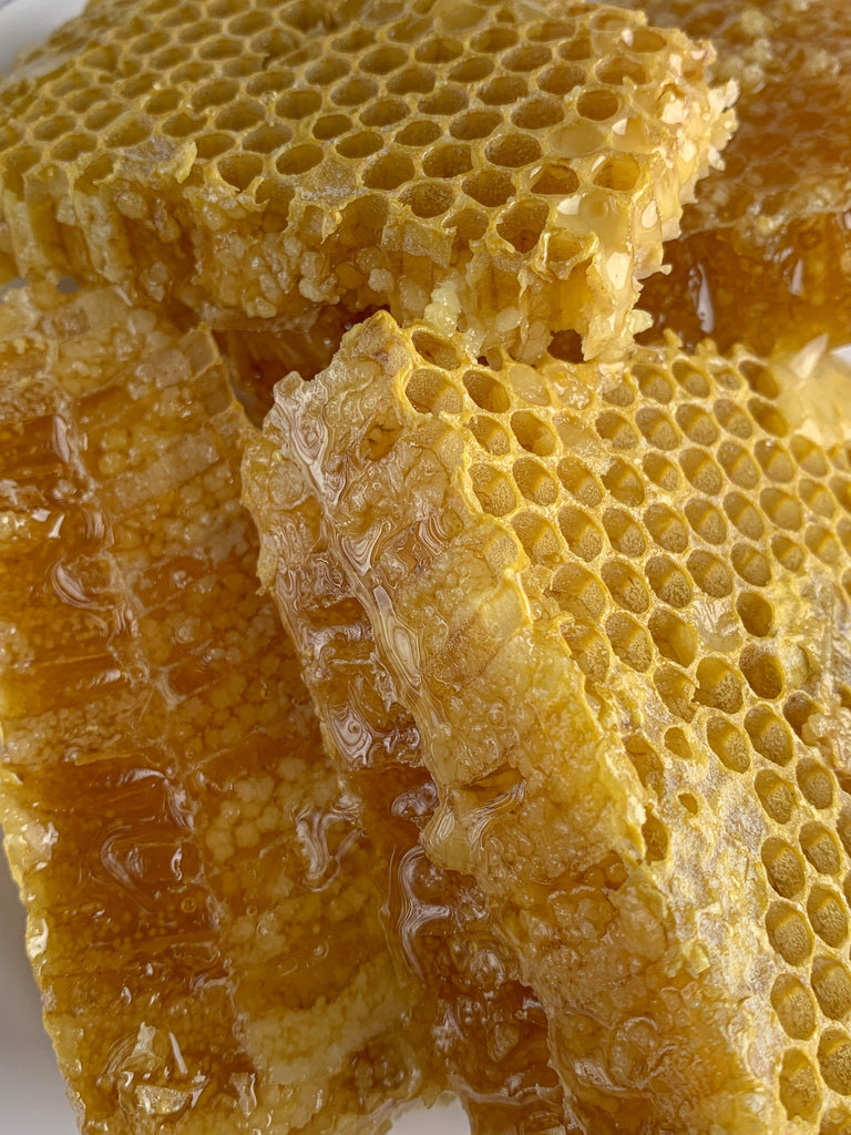 Close-up of raw honeycomb sections dripping with golden honey, illustrating the natural state before crystallization.